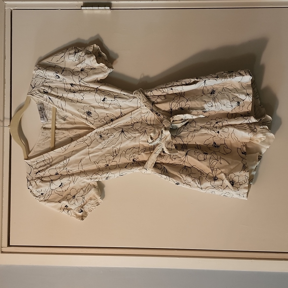 Off-white romper with black floral design and a belt made of the same material.